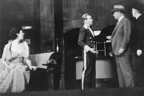 A hat-check boy (Myron McCormick) is questioned about some missing jewelry belonging to a theatre patron (Ilka Chase).