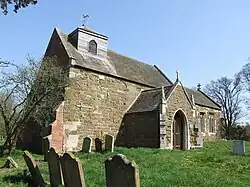 A stone church with a slate roof seen from the southwest, showing the weatherboarded bellcote and the gabled south porch