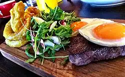 Steak and eggs at a restaurant, with salad and onion rings