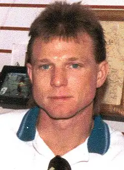 A young man with blue eyes is wearing a white polo shirt with sunglasses hanging from the collar.