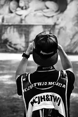 Image 81A man wearing a leather Supreme snapback hat while taking a photograph in 2016 (from 2010s in fashion)