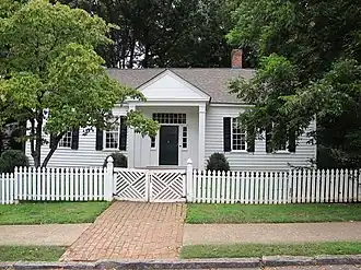 Photo of a one-story home painted white with black shutters with a white picket fence in front.