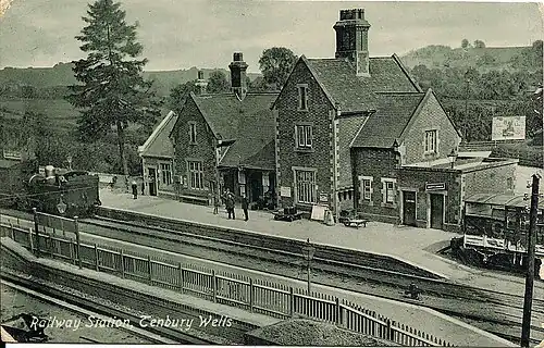 A black and white image of Tenbury Wells railway station, the station buildings and platform can be seen from an elevated angle above another platform below the camera.