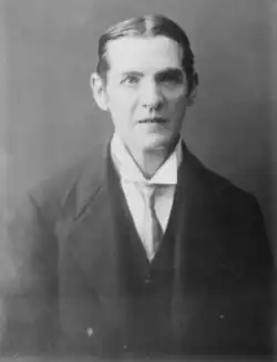 A black and white portrait of a formally dressed individual with neatly combed hair and a serious expression.