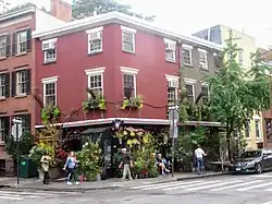 Brick corner building covered in lush plants on the ground floor and second-floor window boxes.