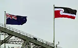 The black, white and red Tino Rangatiratanga flag and New Zealand national flag flying above a bridge
