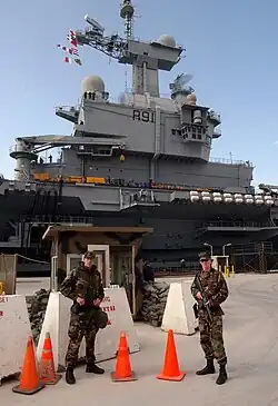 The Naval Support Activity Souda Bay's Security Department soldiers stand a security watch in front of the French aircraft carrier FS Charles DeGaulle (R 91) as it docks at the Marathi NATO pier facility in Souda Bay.