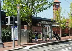 The platform of Union Station/NW 5th & Glisan station with riders waiting near the shelter and the Portland Union Station clock tower in the background