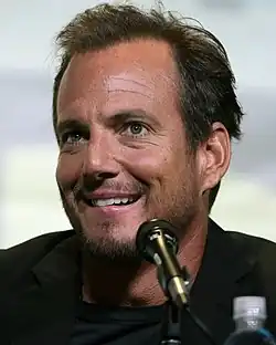 A smiling man in front of a microphone and a water bottle