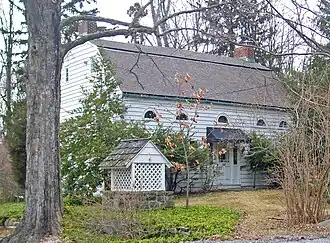 A white wooden house with a gambrel roof, two brick chimneys and semicircular windows