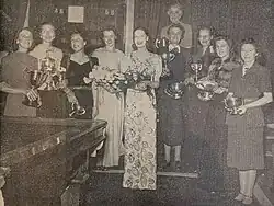 a group of women, some holding trophies, standing next to a billiard table