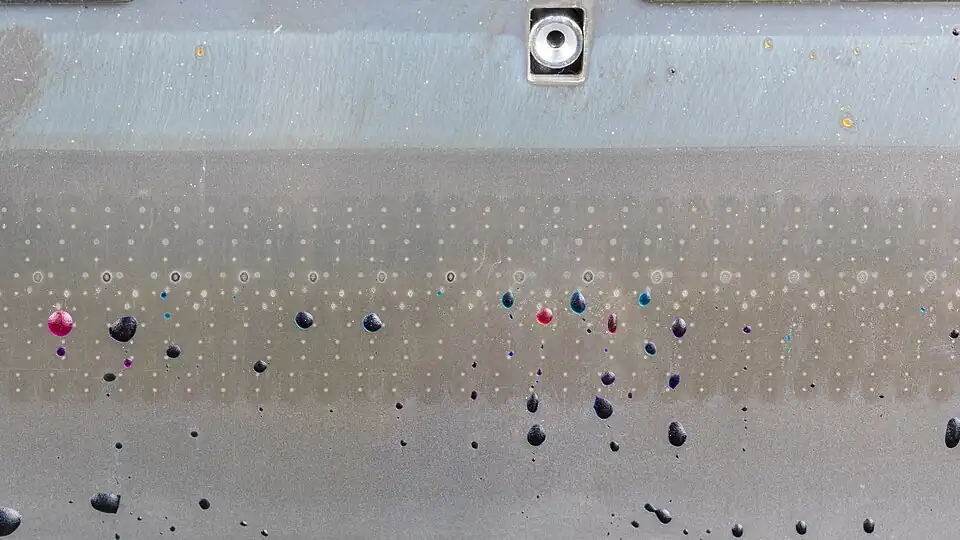 rows of tiny holes in a metal plate, with solidified drops of red and blue wax