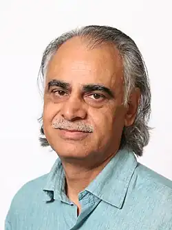 close-up of Ziauddin Sardar wearing a light blue shirt, looking at camera with slight smile